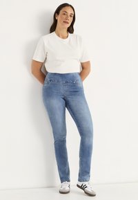 Ljusblå denimjeans med hög midja och två framfickor, i kombination med en vit t-shirt med kort ärm och vita sneakers.