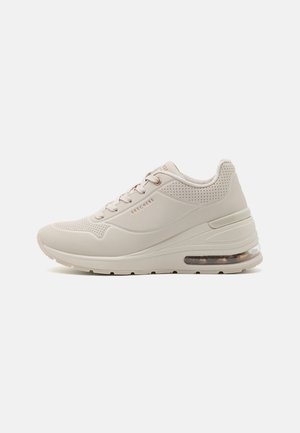 Beżowy sneaker Skechers z wiązaniem z przodu, perforowanymi detalami, grubą podeszwą oraz widoczną poduszką powietrzną w pięcie, widziany z boku.