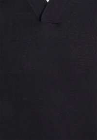 Gros plan sur un tissu tricoté noir texturé avec un motif géométrique subtil et un col en V côtelé.