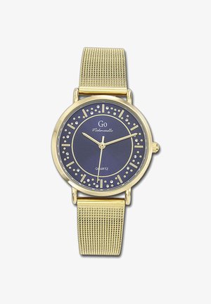 Montre avec un bracelet en maille dorée et un cadran bleu marine, comportant des marqueurs d'heure en argent et des cristaux. Mouvement à quartz indiqué sur le cadran.