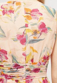 Robe fleurie en tissu pêche clair ornée de fleurs vives pink, violettes et jaunes. Taille froncée et fermeture à bouton au dos.