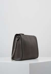 Szara torebka z plisowaniem o wyraźnie zarysowanym kształcie, z łańcuszkiem i czarnymi detalami na brzegach. Gładka tekstura i subtelny połysk.