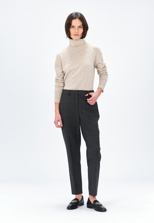 Beige coltrui, grijs geruite broek, zwarte loafers met gouden accenten. Materiaal lijkt een zachte brei; de broek heeft een getailleerde pasvorm.