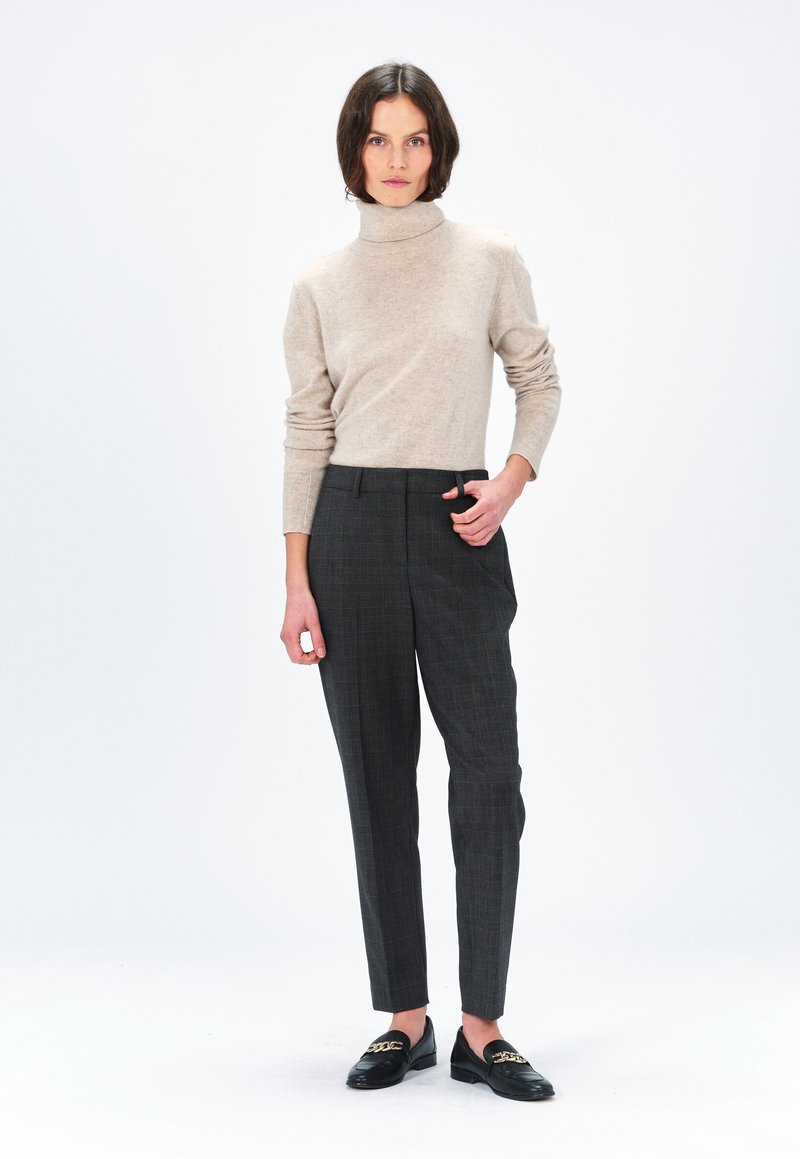 Maglione collo alto beige, pantaloni a quadri grigi, mocassini neri con accenti dorati. Il materiale sembra un morbido maglione; i pantaloni presentano una vestibilità su misura.
