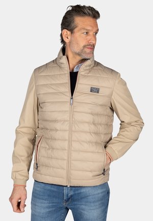 Beige, pufferstijl jas met een hoge kraag, ritssluiting en zijzakken. Heeft contrasterende bies op de manchetten en een logo patch op de borst.