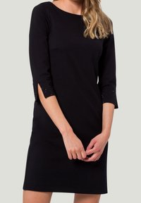 Robe noire à manches trois-quarts avec découpes et accents embellis. Le tissu semble doux et ajusté à la taille.