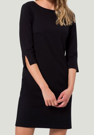 Robe noire à manches trois-quarts avec découpes et accents embellis. Le tissu semble doux et ajusté à la taille.