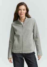 Grijze ritsjack met een textuurpatroon, rechte pasvorm en twee zijzakken, gecombineerd met donkere spijkerbroeken.