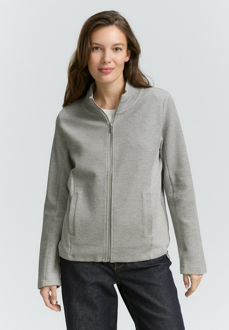 Grijze ritsjack met een textuurpatroon, rechte pasvorm en twee zijzakken, gecombineerd met donkere spijkerbroeken.