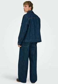 Temno modra denim jakna in usklajene široke kavbojke, z vidnim šivanjem, zapiranjem na gumbe in dvema zadnjima žepoma.