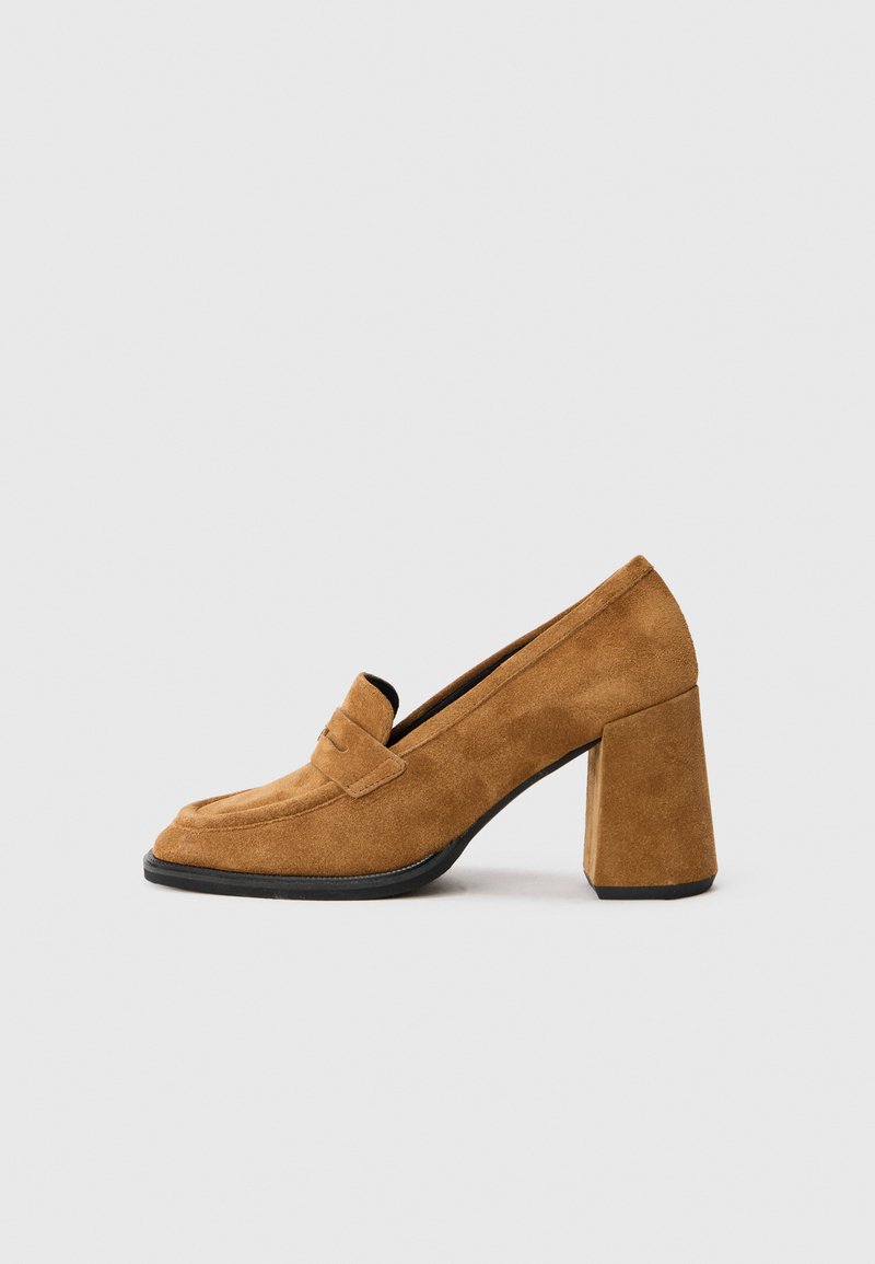Mocassino in suede marrone con tacco a blocco, punta arrotondata e dettagli di cucitura sulla fascia, mostrato su sfondo bianco semplice.