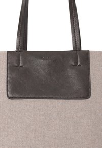 Una borsa tote elegante con un corpo in tessuto beige testurizzato e una patta in pelle marrone scuro liscia con un branding discreto. Due manici robusti completano il design.