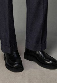 Mustad nahast loafers, millel on sile pind ja kummist tald, koos tumedate kalasaba mustriga pükstega, mille sääred on üles keeratud.
