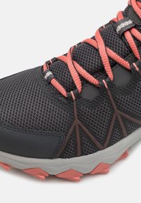 Gros plan d'une chaussure de sport en mesh gris avec des lacets corail, des détails de semelle corail et marron, et une semelle intermédiaire blanche.