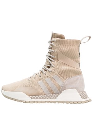 Beige high-top sneaker with knitted upper, lace-up front, three stripes on side, textured midsole, and pull tab at the back.
