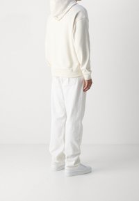 Felpa crema con una vestibilità rilassata e una consistenza morbida, abbinata a jeans bianchi larghi e sneakers bianche, vista da dietro.