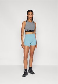 Szürke crop top fekete "PRO NIKE" pánttal, világoskék sportnadrággal párosítva. A modellen fekete, textúrázott mintázatú sportcipők vannak.