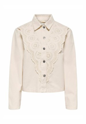 Blouse longue manches longues couleur crème avec fermeture à boutons sur le devant et détail en dentelle œillets festonnée en forme de V sur la poitrine et les épaules.