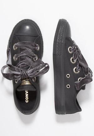 Paar schwarze Sneaker mit niedrigem Schaft, dicken Samtband-Schnürsenkeln, Gummikappen an den Zehen sowie strukturierten Gummisohlen auf weißem Hintergrund.