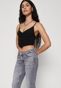 Fekete bordázott crop top, ráncolt részletekkel, világoskék, illeszkedő farmernadrággal párosítva. Figyelemre méltó ezüst lánc nyaklánc és minimális kiegészítők.