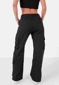 Pantalon cargo noir à coupe décontractée, avec plusieurs poches, des passants pour ceinture et une coupe droite des jambes. Le tissu semble solide et texturé.