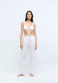 Bela bomba z bombažem s tankimi naramnicami, v kombinaciji s svetlo sivo črtastimi širokimi pižamami, ki imajo pas z logotipom Calvin Klein.