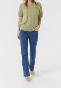 Olivgrön stickad kortärmad tröja med texturerade prickar, tillsammans med blå raka jeans och beige spetsiga skor.