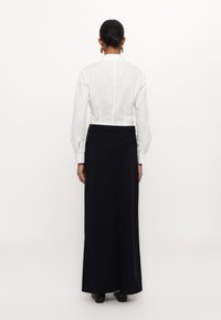 Balta garām piedurknēm kreklā ar pieguļošu muguru, saskaņota ar elegantu jūras zila maksi svārki. Svārki ir ar nelielu aizmugurējo šķēlumu un minimālām detaļām.