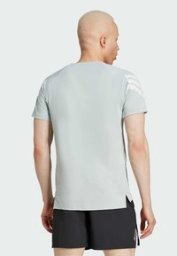 Camiseta atlética gris claro de manga corta, con un tejido texturizado y franjas blancas en los hombros. Combinada con pantalones cortos negros.