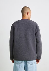 Mørkegrå fleece sweatshirt med en blød tekstur, løstsiddende pasform og rund halsudskæring, båret over lyseblå jeans med minimale designdetaljer.