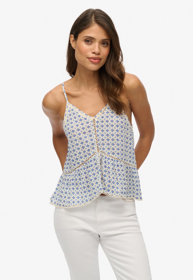 Lichtblauwe en witte gepatroonneerde camisole met een uitlopende zoom en kantdetails. Spaghetti-bandjes en knoopaccenten aan de voorkant.