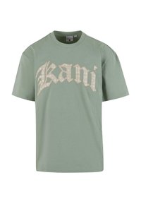 Mint green cotton t-shirt with oversized fit, featuring large, decorative cream-colored text "Kani" across the front. Short sleeves, round neckline.