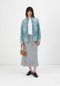Lyseblå denimskjorte med knappeåpning, hvit topp under, svart-hvitt stripet skjørt, svarte loafers og en liten brun håndveske.