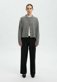 Grau gestrickte Strickjacke mit rundem Ausschnitt, gerippten Bündchen und sechs goldenen Knöpfen. Über einem weißen Hemd getragen und kombiniert mit schwarzen, weit geschnittenen Hosen.
