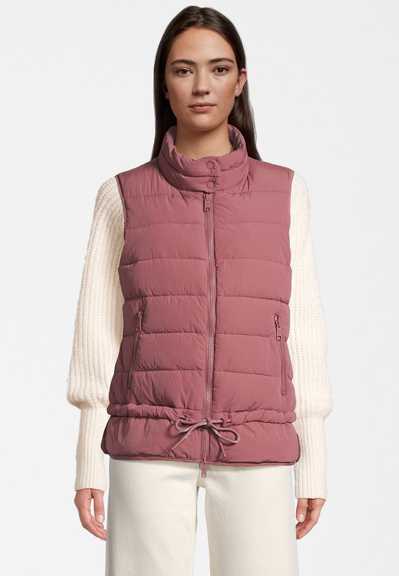 Padded vest w jasnym mauve z wysokim kołnierzem, zamkiem z przodu i regulowanym ściągaczem w pasie. W zestawieniu z kremowym swetrem.
