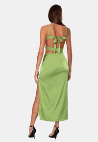 Groene satijnen jurk met een aansluitend silhouet, spaghettibandjes, open rug en een hoge split aan één kant. Touwtje achter voor sluiting.