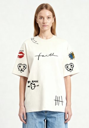 Jeune femme porte une chemise blanche oversize avec des mots manuscrits noirs et des motifs graphiques comprenant « faith », des cœurs, des lèvres, le soleil et des marques de comptage.