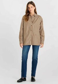 Bruin-wit gestreept overhemd met knopen en lange mouwen, losse pasvorm, gecombineerd met een blauwe spijkerbroek en zwarte schoenen. Gladde, geweven textuur.