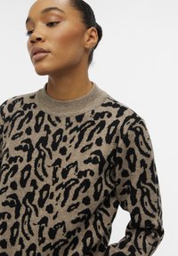 Pull en imprimé léopard avec une base beige, des motifs noirs et un col rond côtelé. Texture douce et poids moyen.