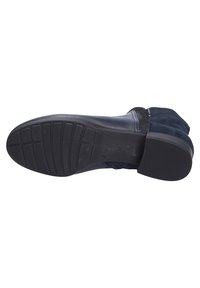 Semelle de chaussure en caoutchouc noir avec un motif de prise texturé, caractérisée par un orteil arrondi et des détails en daim près du bord supérieur. Construction légère.