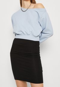 Sudadera ligera azul celeste de hombros descubiertos con dobladillo elástico, combinada con una falda mini negra ajustada, que presenta una textura suave y un detalle mínimo.