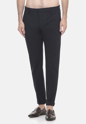 Pantaloni neri su misura con vestibilità slim, dotati di tasche laterali, una texture liscia e orli arrotolati alle caviglie. Indossati con mocassini scuri.