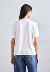 Tricou alb din bumbac cu mâneci scurte și guler rotund, având o croială lejeră și o textură netedă. Purtați cu blugi din denim albastru.