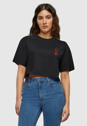 Black cropped t-shirt made of cotton, featuring a red graphic of a "Q" and heart on the left side, paired with blue high-waisted jeans.