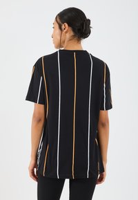 Svart t-shirt med vertikala orange och vita ränder, korta ärmar och en lös passform. Mjukt tyg med rundad hals och sidslitsar.