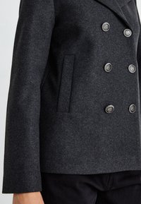 Chaqueta de mezcla de lana de doble botonadura en gris oscuro, con un amplio cuello, botones en tono plateado y detalle de bolsillo lateral. Textura suave.