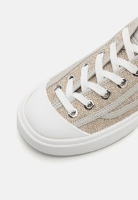 Beige lærduk sneakers med hvit gummisåle, med hvite snørebånd og metalløye. Overdelen har et teksturert mønster med subtile detaljer.