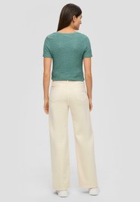 Groene gestructureerde top met korte mouwen, gecombineerd met hoogwaist crèmekleurige wijde broek en witte sneakers, gezien vanaf de achterkant.