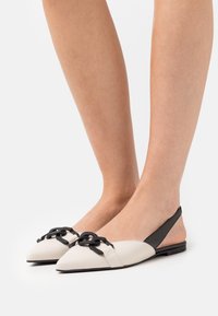 Platta slingback-skor i vit och svart läder, med spetsig tå, kedjeaccent framtill och en minimalistisk design.