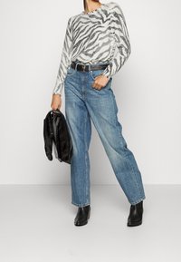 Pull à manches longues avec un motif zèbre en gris sur fond blanc, associé à un jean bleu taille haute. Ceinture noire et bottines à talons ouvertes.